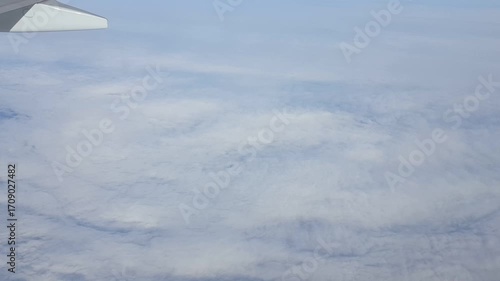 Plane flying above clouds with wing visible from passenger window view.