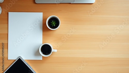 Minimalist office desk with coffee cup and plant, top-down view on warm wooden surface.