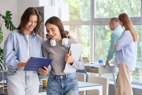 Female students with clipboard and laptop in library