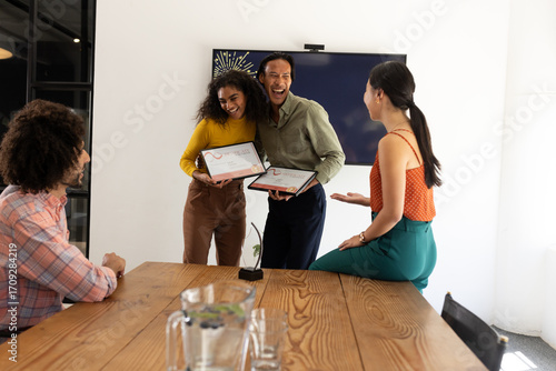 Colleagues celebrating achievement with certificates in modern office meeting room