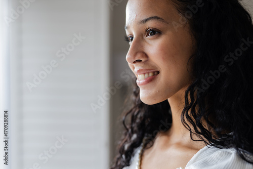 Billede på lærred Smiling woman looking out window, feeling hopeful and inspired at home