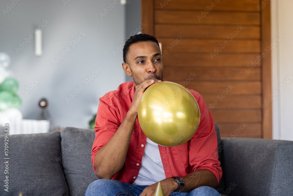 Fototapeta premium Man inflating gold balloon on couch, preparing for festive celebration