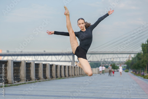 choreography on the street. a young gymnast on a walk shows exercises and stretching by demonstrating the splits in a jump