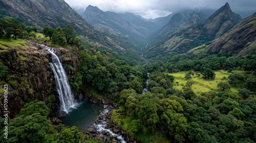 Tall waterfall flowing from the heart of a mountain range, framed by steep slopes and dense greenery