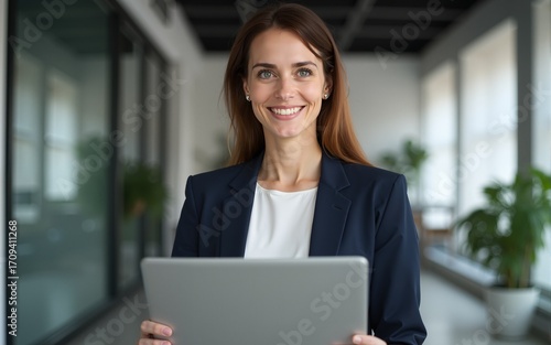 Portrait latin mature adult professional business woman looking at camera and smiling. European businesswoman CEO specialist holding digital laptop pc using fintech app standing at workplace in office