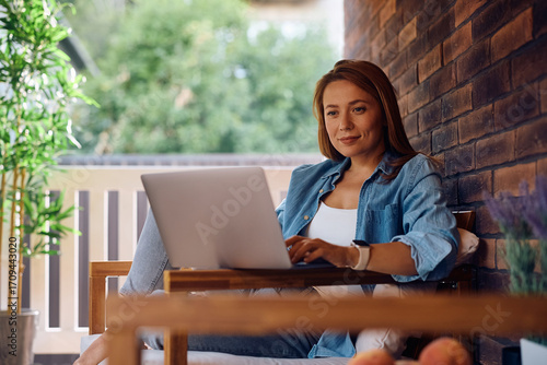 Canvas Print Smiling woman surfing the net on laptop on porch.