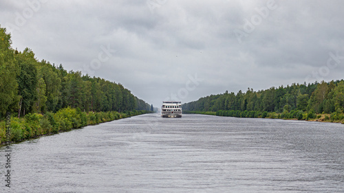 A river passenger ship sails through a canal on the banks of which trees grow