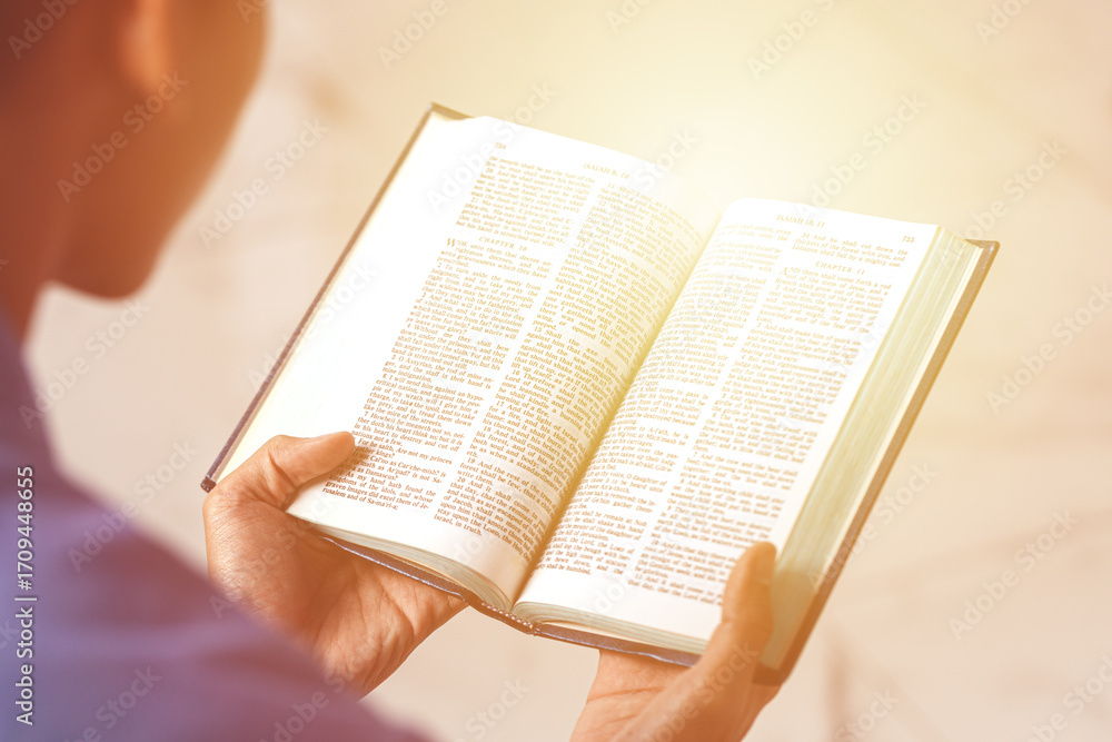 Fototapeta premium Close-up of person holding and reading an open holy book with text, concept of faith, spirituality, wisdom, learning, and inspiration.