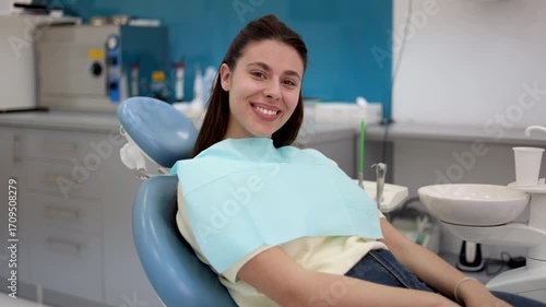 Smiling young woman in a dental chair, awaiting a check-up in a contemporary clinic, exudes satisfaction