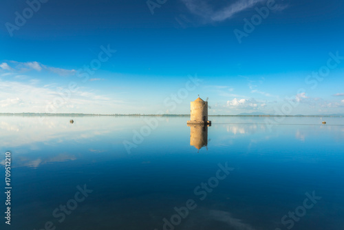 Old spanish windmill reflected in Orbetello lagoon waters, Argentario, Italy.