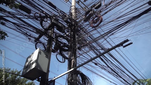Messy power wires are tangled on the electrical pole, creating a chaotic arrangement of internet cables and powerlines in Thailand.	