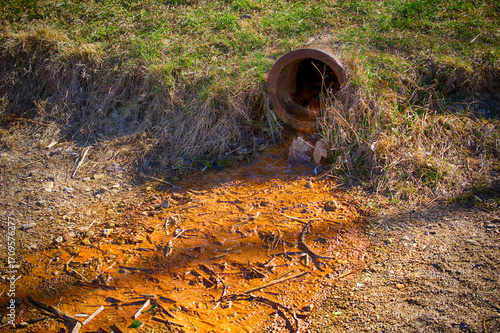 A rusty pipe releases polluted water, showing environmental contamination and water waste.