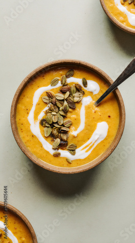Butternut squash soup in a kraft bowl with seeds and cream swirl on a pastel sage background, slight overhead studio shot