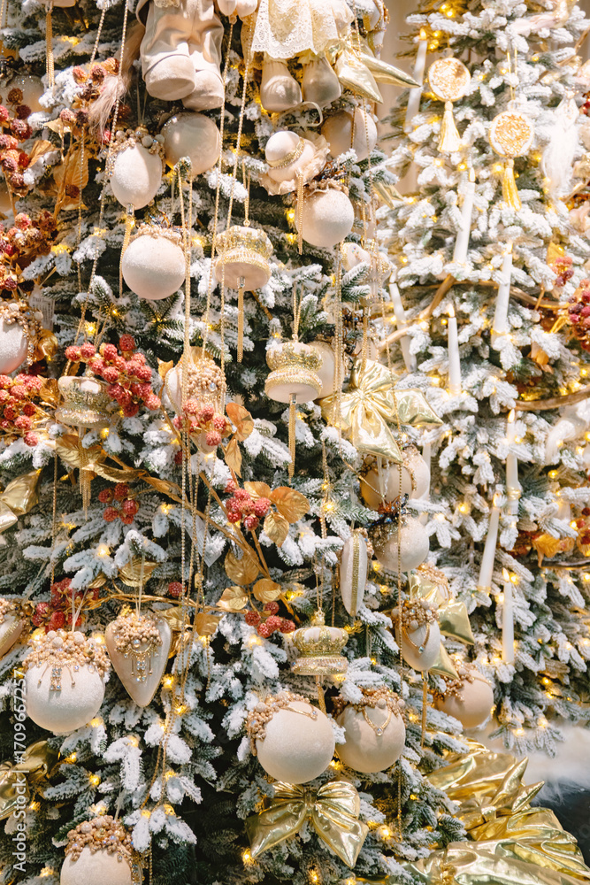 Fototapeta premium Elegant Christmas tree adorned with lavish gold, cream ornaments, and festive red berries, flocked with snow for a luxurious winter holiday display.