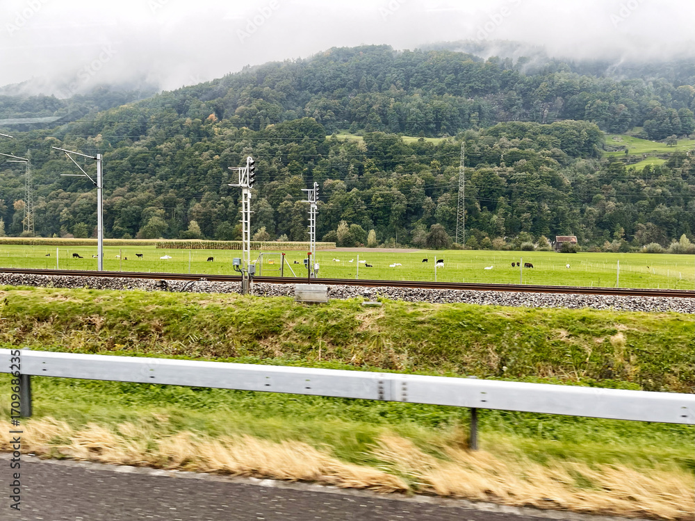 Fototapeta premium Peaceful Swiss countryside with green fields, mountains, and railway infrastructure