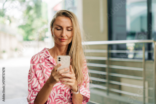 Young blonde woman using mobile phone to chat while standing outside.