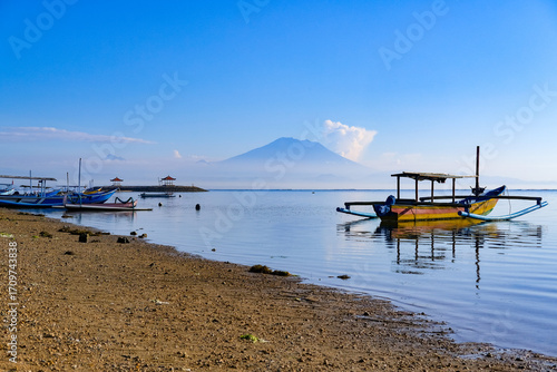 Bright morning at Sanur Beach with golden sand and a traditional boat on calm waters, horizon stretching beneath a clear blue tropical sky for a peaceful seaside escape.