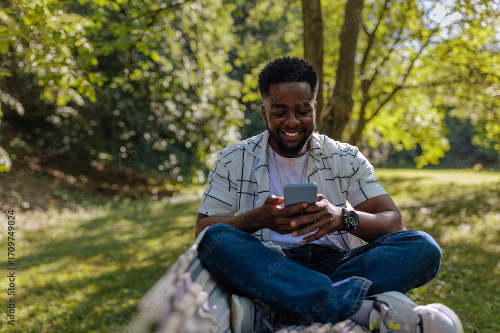 Fototapeta premium Man sitting in a hammock looking at the phone in his hands