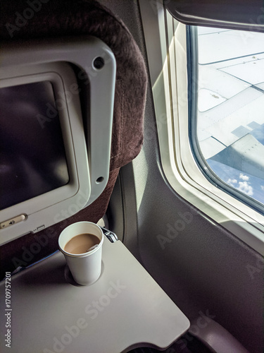 Coffee cup on an airplane tray beside the window, with a clear view of the aircraft wing under bright daylight during flight.