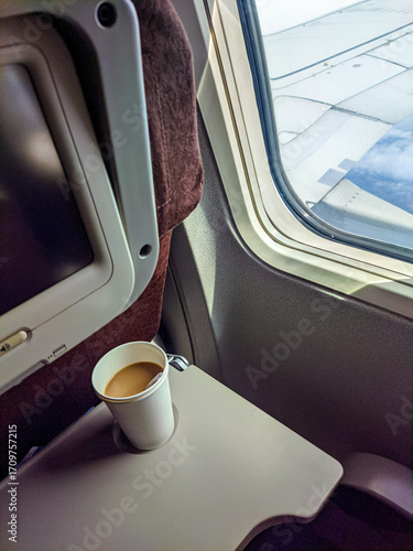 Coffee cup on an airplane tray beside the window, with a clear view of the aircraft wing under bright daylight during flight.