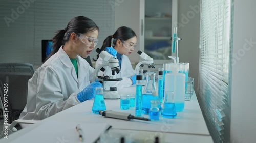 Scientists working with microscopes and blue liquids in laboratory