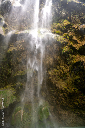 An unusual tropical waterfall. Thin streams of water flow down the mossy stone terraces into the turquoise lake. Cebu. Tumalog Falls.