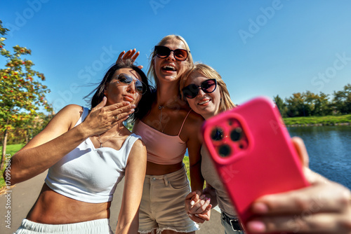 Fotografie Three friends taking a selfie outdoors by the river in sunny weather