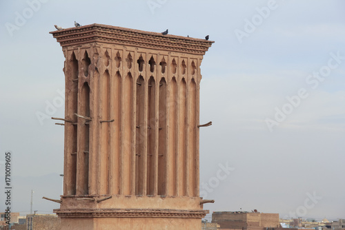 Historic windcatcher tower in Yazd, Iran, featuring traditional Persian mudbrick architecture and desert heritage against a cloudy sky.