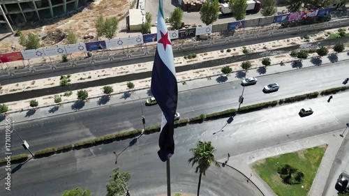 An aerial view captures the new Syrian national flag hoisted on a towering pole in central Damascus, with Mount Qasioun, one of the capital’s most prominent landmarks rising in the background.