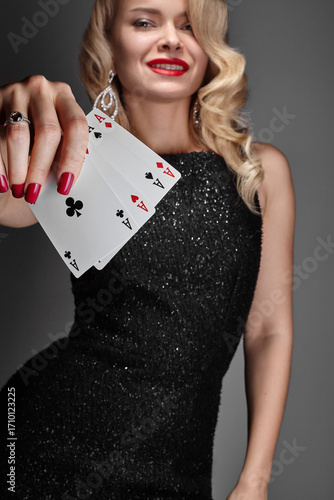 Blonde lady woman in black shiny dress and expensive diamond jewelry is winner money from Omaha Holdem. She is smiling, showing Aces cards to the camera. Ideal style for Poker, Casino, Gambling.
