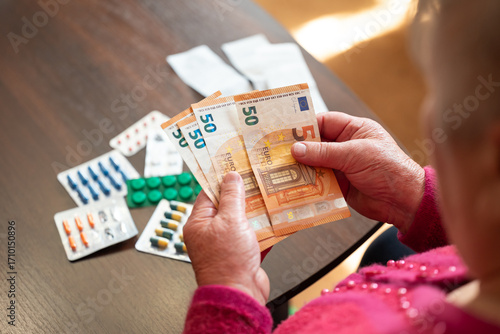 An elderly woman counting euros near medication. A grandmother counts money against a background of medicines, a symbol of the high cost of medicines and the lack of funds in Europe
