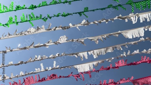 Colorful red, white, and green paper decorations for a street party waving in the wind against a clear blue sky on a sunny day