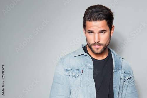 Handsome young man with dark hair and beard posing in casual clothes