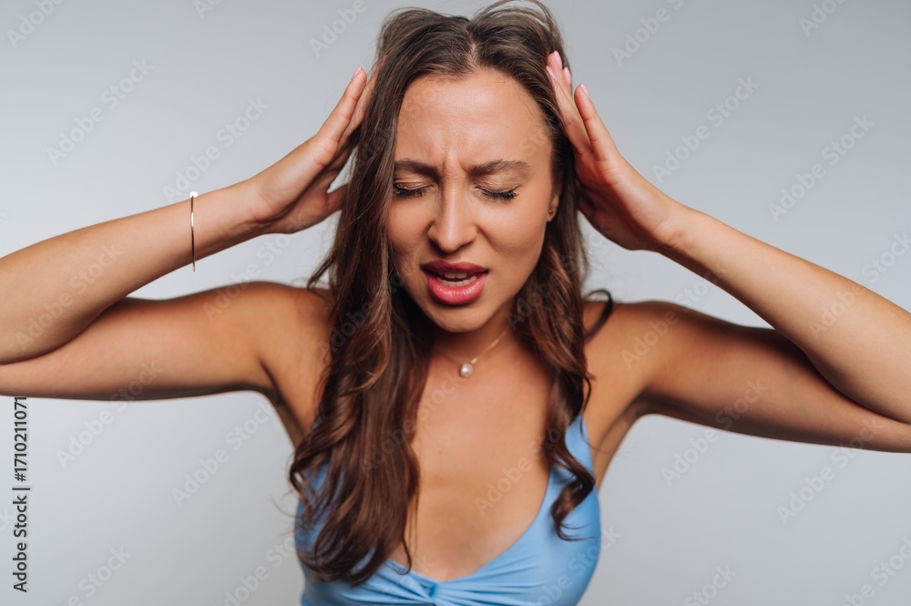 Fototapeta premium Young woman expresses frustration while holding her head in a studio setting