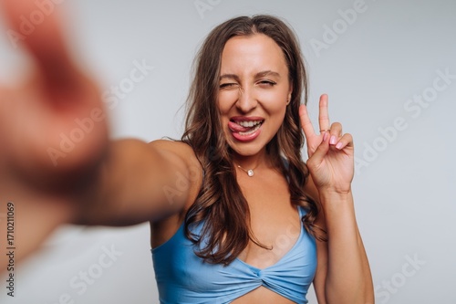 Young woman posing playfully with peace sign and sticking out tongue indoors