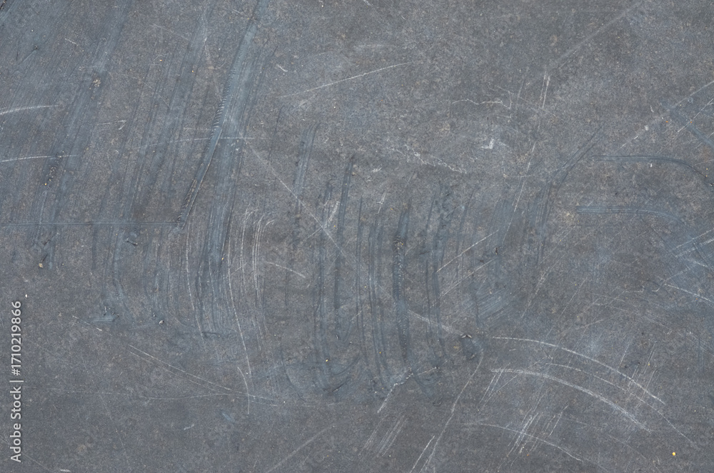 Fototapeta premium A close-up of a heavily scratched and scuffed dark gray surface, featuring light-colored abrasions and arcing scrapes, perfect for a rugged, worn background.