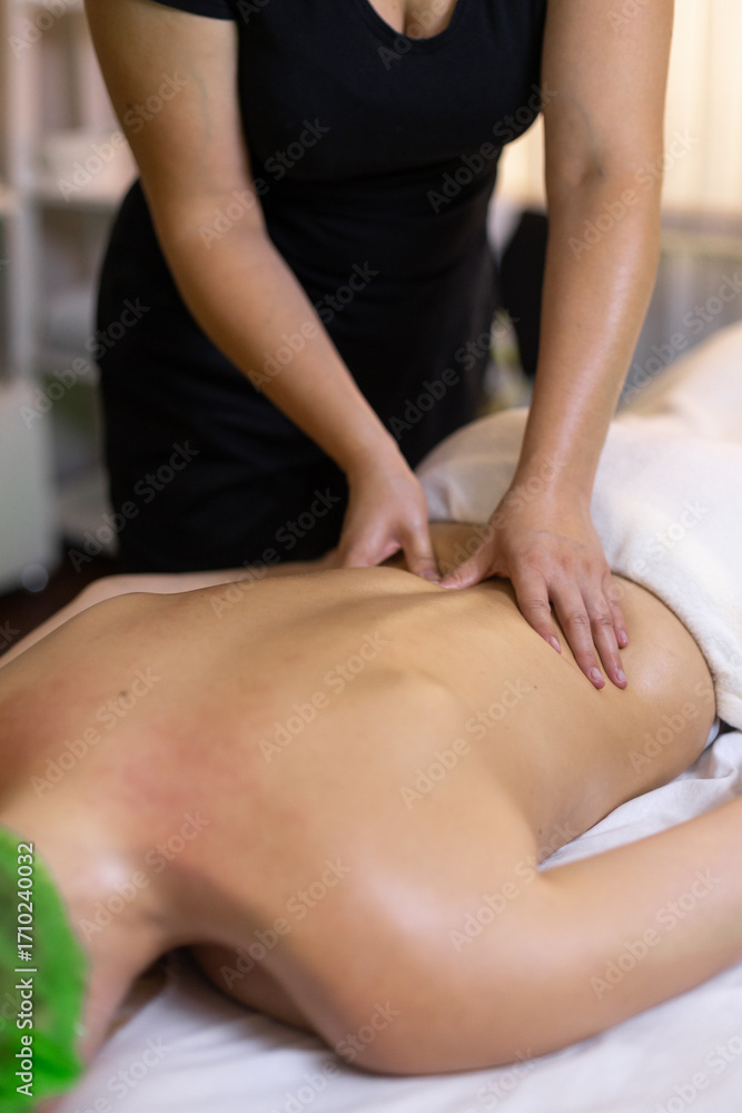 Fototapeta premium Massage therapist applying pressure with fingers to a client’s lower back muscles on a treatment table