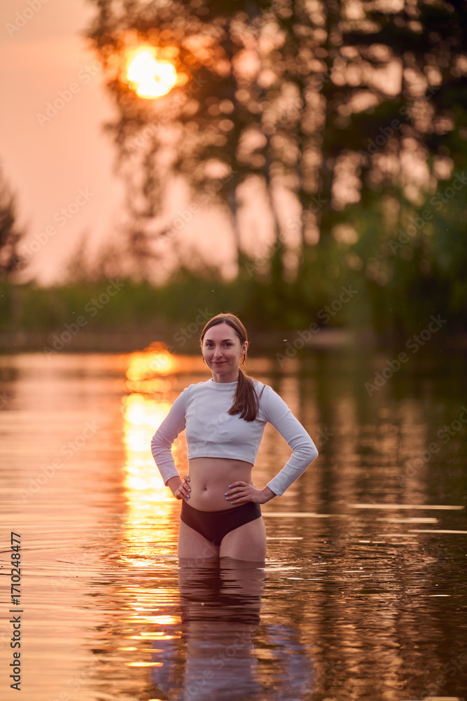 Fototapeta premium Young woman enjoys water at sunset