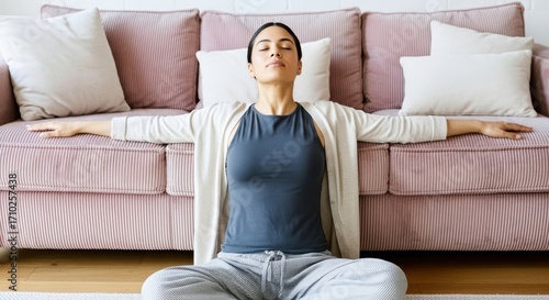 Calm woman meditating at home, practicing mindfulness for stress relief and mental wellness. Peaceful woman relaxing in a yoga pose on the floor of her modern living room, self-care and well-being.
