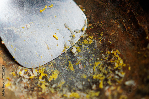 Close-up shot presenting metal spatula with remnants on a textured surface, creating an abstract and textured composition, carefully isolating the subject against a bright background.
