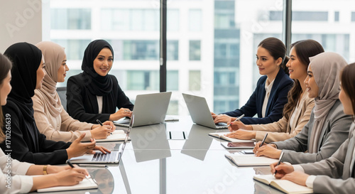 A group of diverse, professional businesswomen, including those in hijabs, in a corporate meeting. This image is perfect for themes of teamwork, diversity, and female empowerment in the workplace.
