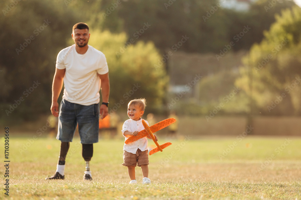 Obraz premium Running with toy plane, imagination. The amputee father is with his son on the field