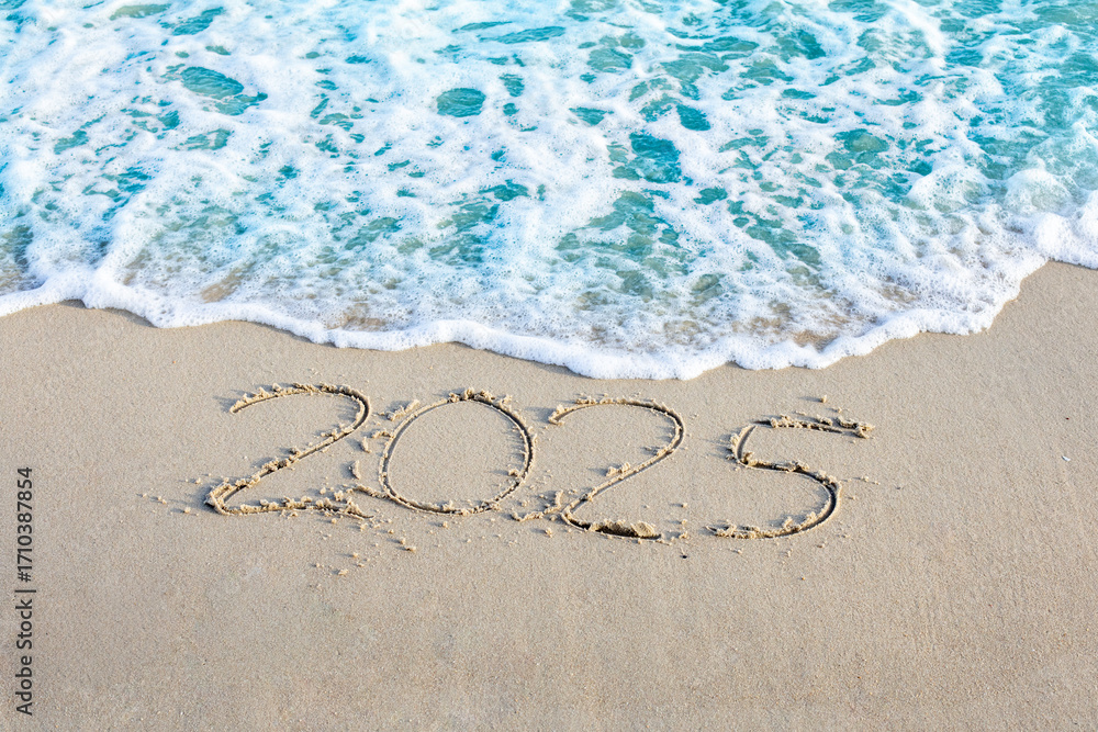 Fototapeta premium 2025 written in sand with ocean waves approaching, symbolizing passage of time and new beginnings