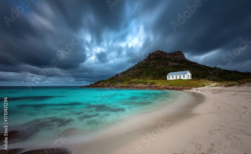 A small white house sits on an island in the middle of light blue waters