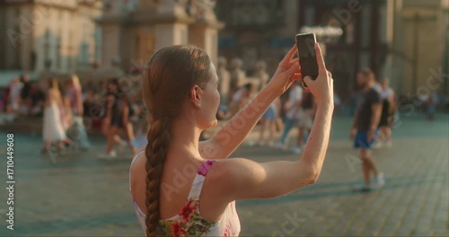 Woman takes a selfie in a historic European city square, capturing the warm glow of the golden hour sunset