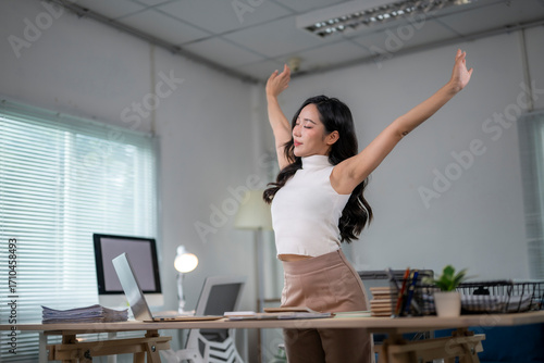Asian businesswoman stretching arms at workplace after work is done