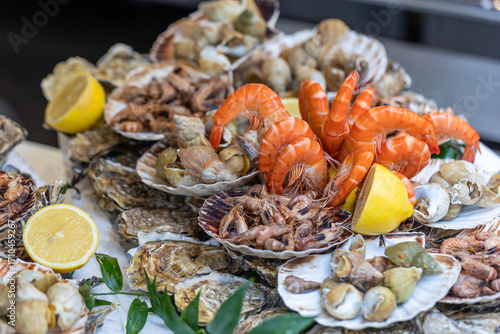 A large seafood platter with a variety of fresh seafood, including oysters, whelks, shrimp, prawns, and scallops, is a presentation of the market's assortment and a tasting set in Paris, France.