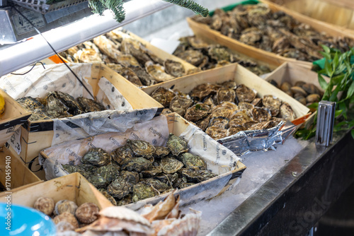 Fototapeta Naklejka Na Ścianę i Meble -  Fresh oysters are for sale in a wooden crate at a street seafood market in Paris, France. One oyster is open, revealing the meat inside.