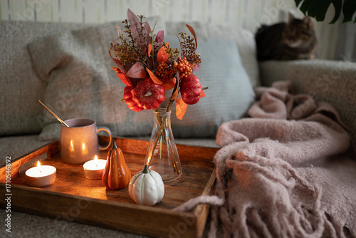 Cozy composition with cup of tea on the wooden tray, interesting book, candles and warm blanket. Hygge home interior. Selective focus.
