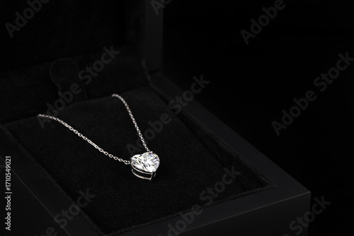 A heart shaped pendant with a chain is displayed in a black box